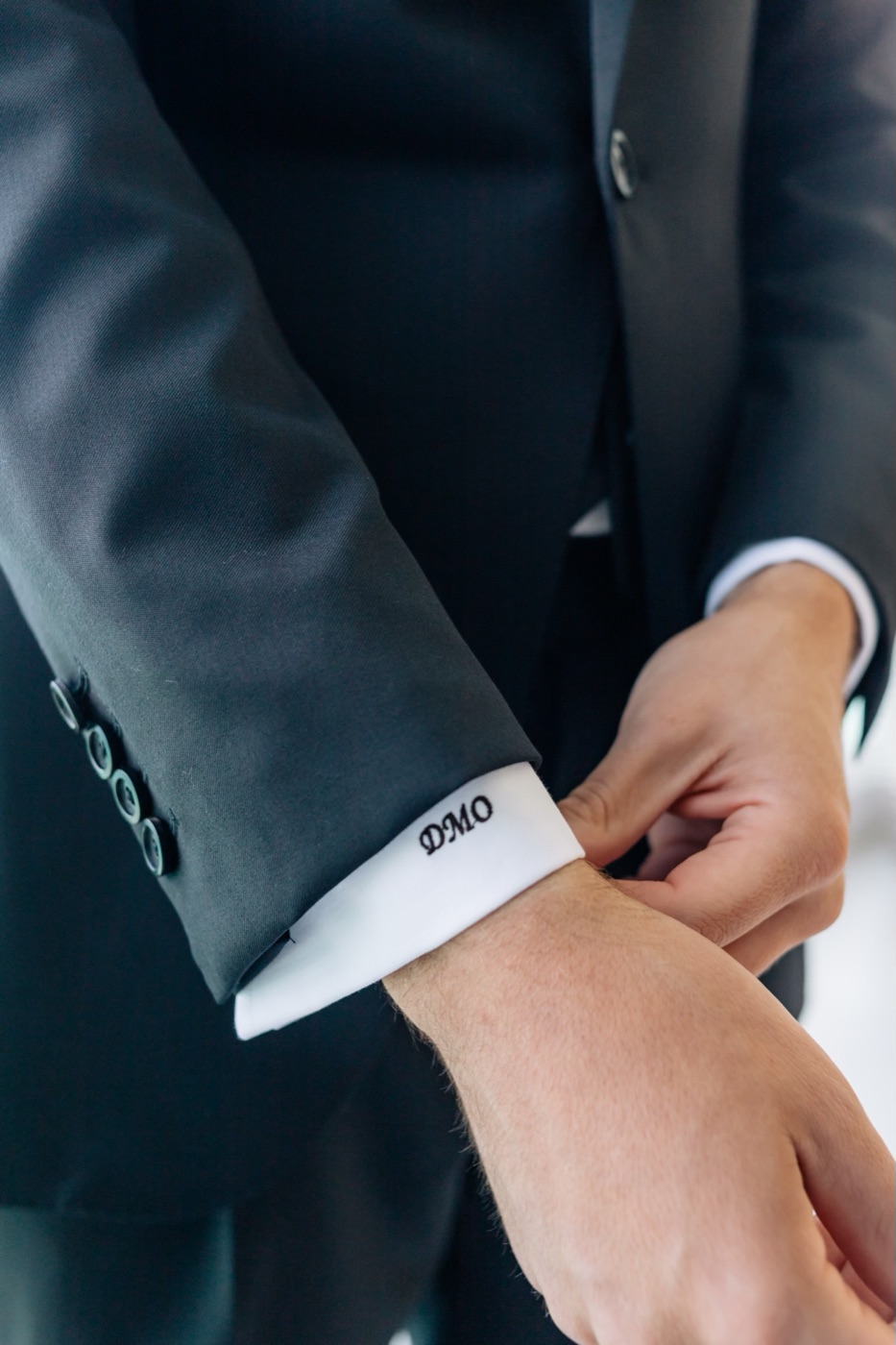 Monogrammed DMO shirt cuff beneath a black jacket sleeve
